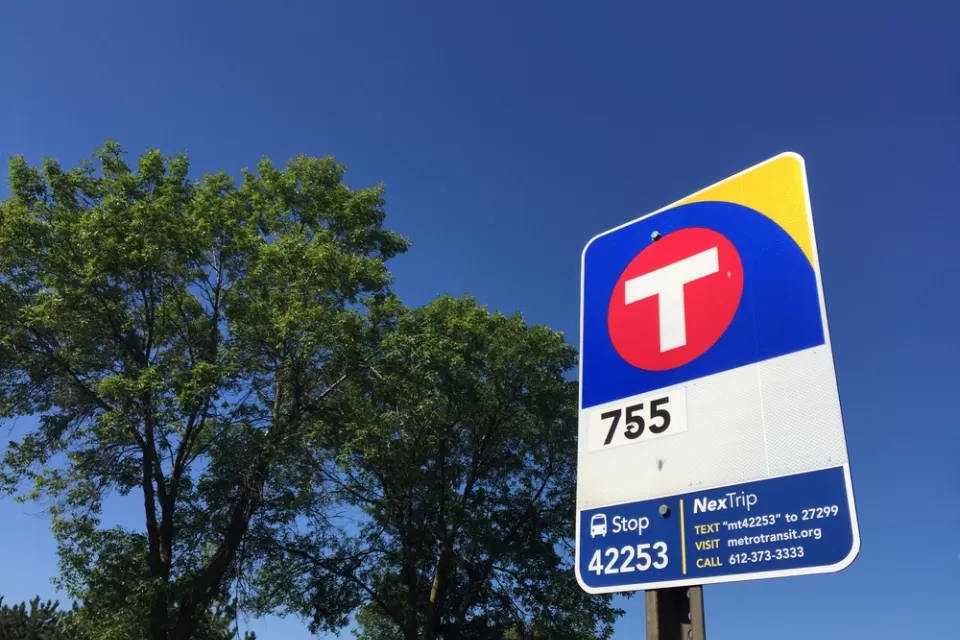 Close-up of red and blue MetroTransit bus stop sign against blue sky and green tree in New Hope, Minnesota